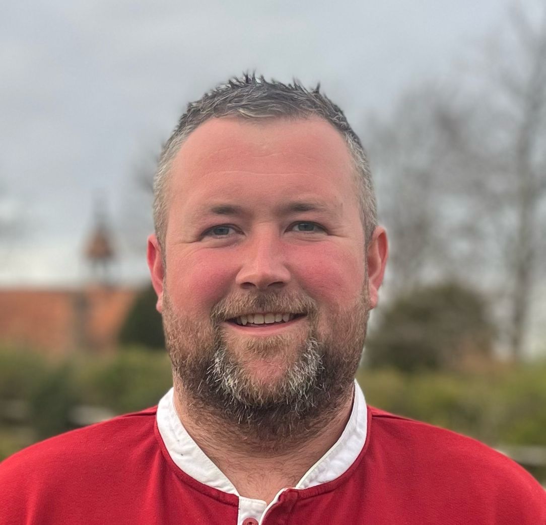 Headshot of a man wearing a red top with white collar.